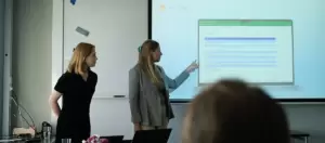 Två personer presenterar sitt arbete, de står längst fram i salen och pekar på presentation
